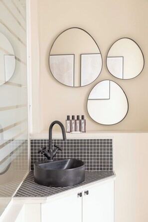Une salle de bain avec un lavabo noir, un miroir et trois miroirs ronds fixés au mur.