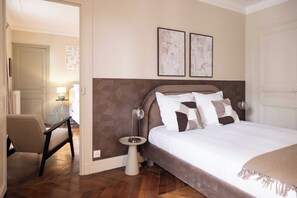 Une chambre à coucher comprenant un lit, une chaise, une table de chevet avec une lampe, et deux tableaux encadrés accrochés au mur.