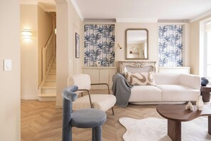 Un salon avec un canapé blanc, un fauteuil bleu, une table basse en bois et un mur orné d’un motif.