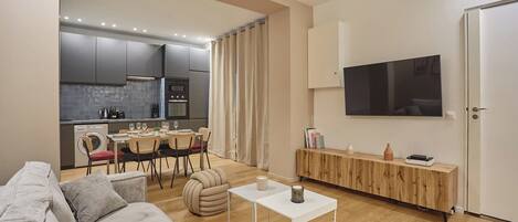 A modern living room with a grey sofa, a small white table, and a dining area with a table and chairs.