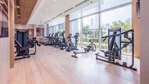 A modern gym with various exercise equipment, large windows, and a city view.