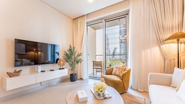 A modern living room with a flat-screen TV, a sofa, a coffee table, and a sliding glass door leading to a balcony.