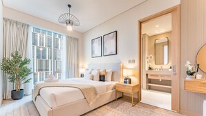 A modern hotel room with a large bed, bedside tables, a potted plant, and a bathroom with a mirror and sink.