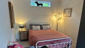 A neatly arranged bedroom with a bed, bedside table, lamp, and a window with a view of a dog.