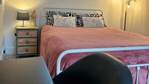 A bedroom with a bed, a desk, a chair, a nightstand, a lamp, a floor lamp, and a window with a dog silhouette.