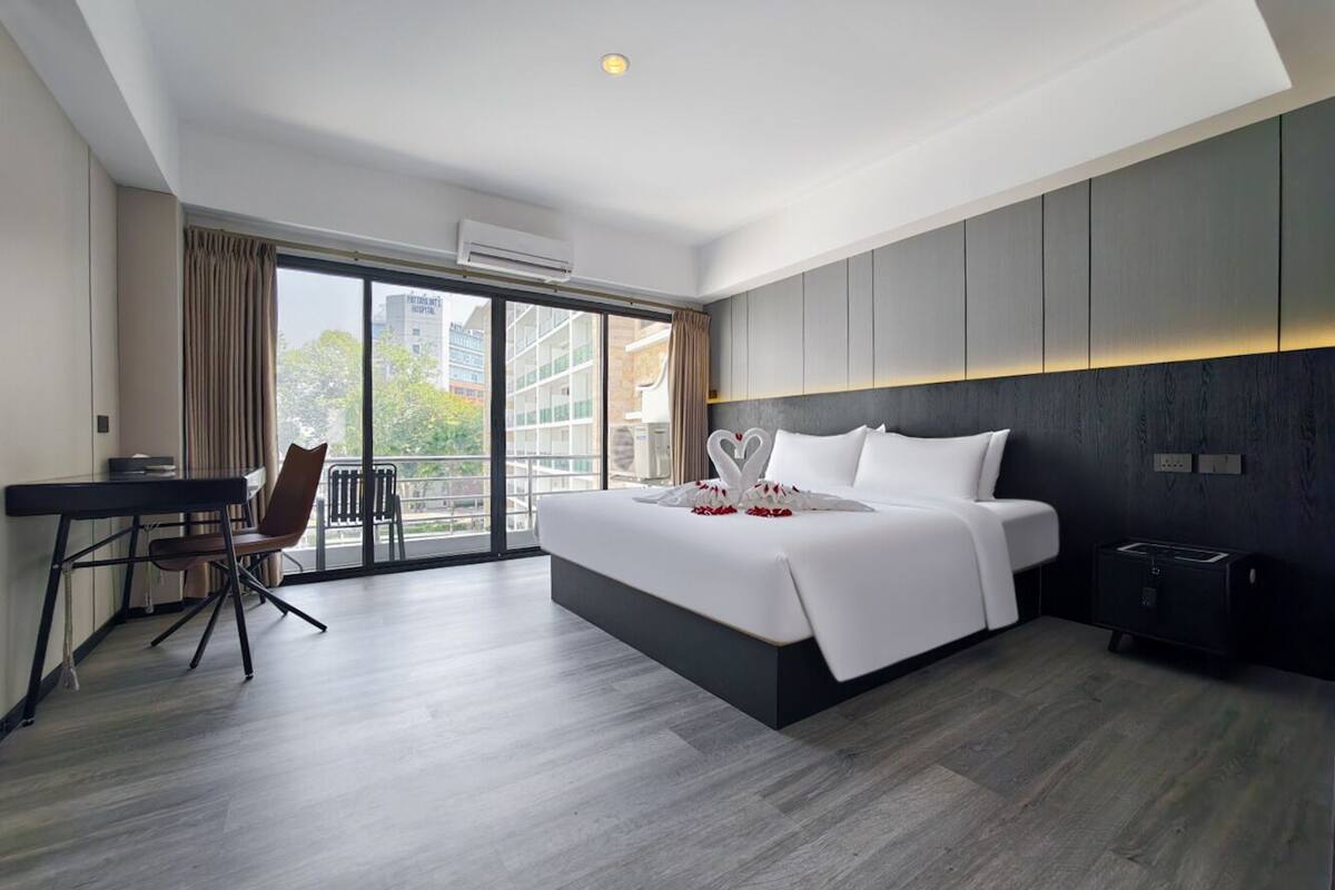 A modern hotel room with a large bed, a desk, and a view of the city.