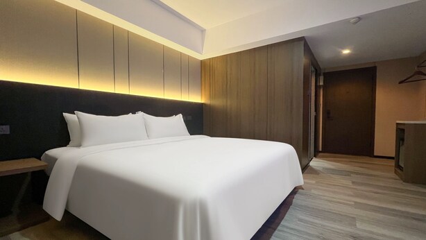 Et moderne hotelværelse med en stor seng, et træhovedgærde og en indbygget garderobe.