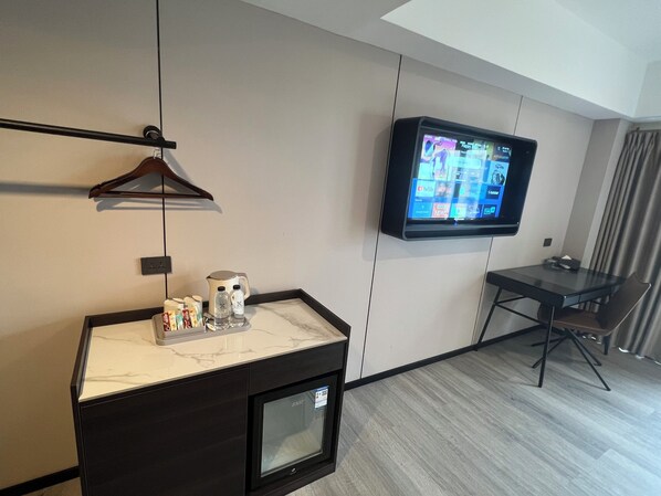 A hotel room with a flat-screen TV mounted on the wall, a small table with a kettle and condiments, and a chair. - X Hotel Pattaya (Pattaya)