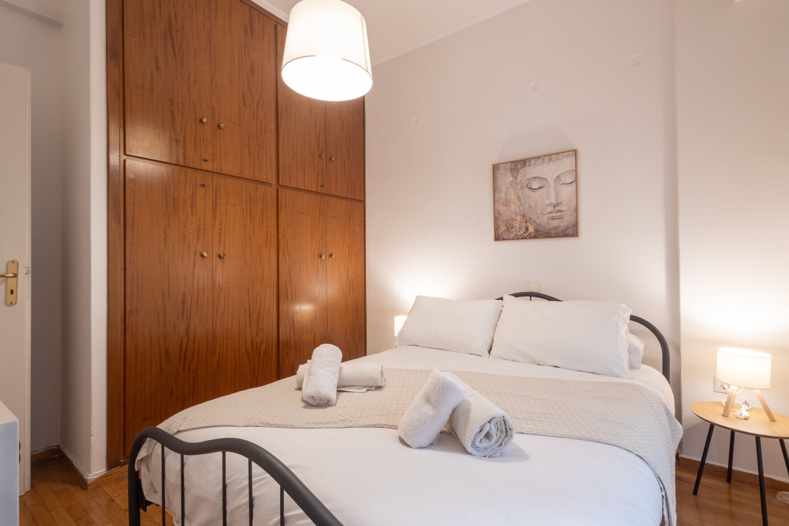 A bedroom with a bed, wooden wardrobe, and a wall-mounted artwork.