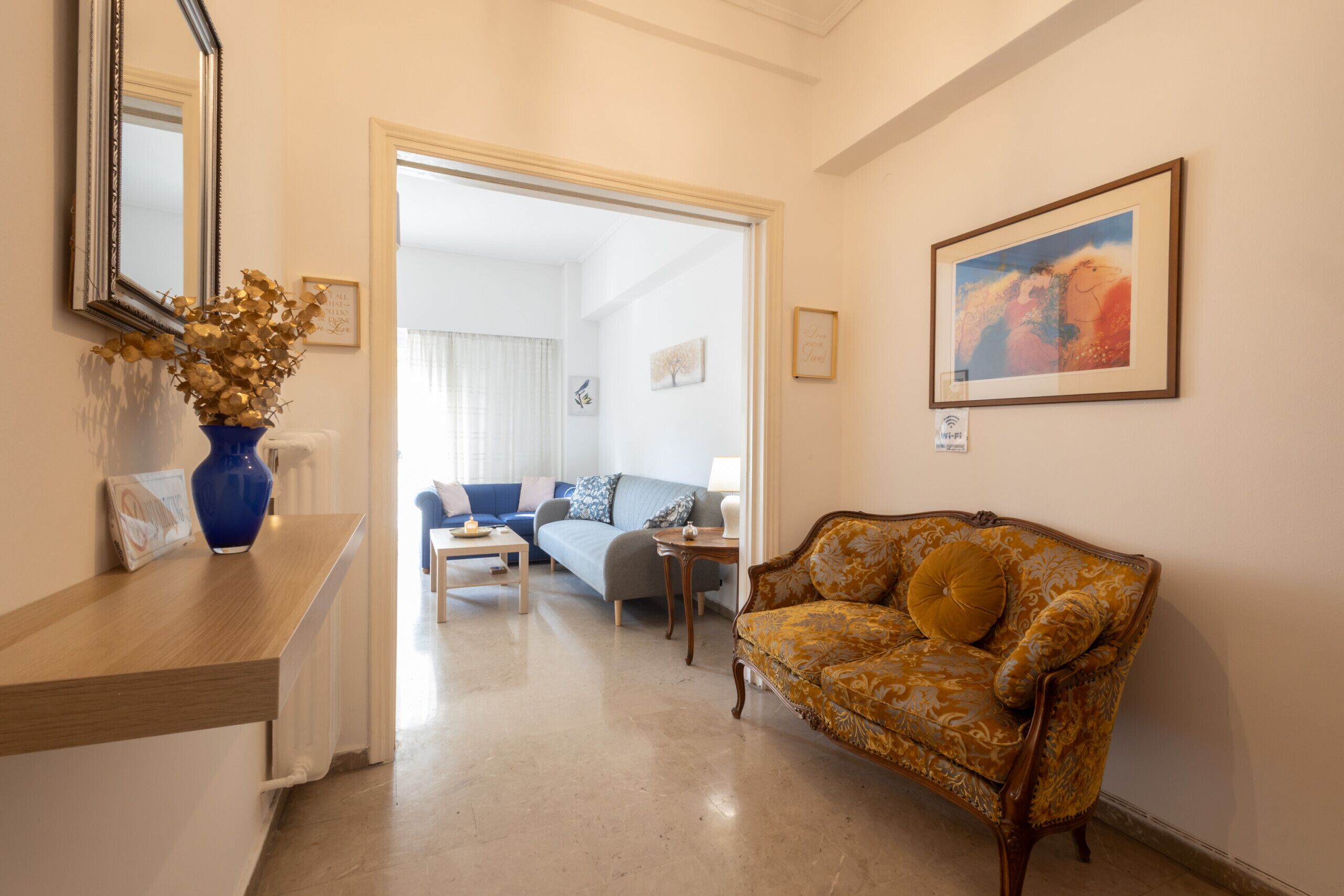 A hotel lobby with a wooden reception desk, a blue vase with dried flowers, a patterned sofa, and a framed painting on the wall.