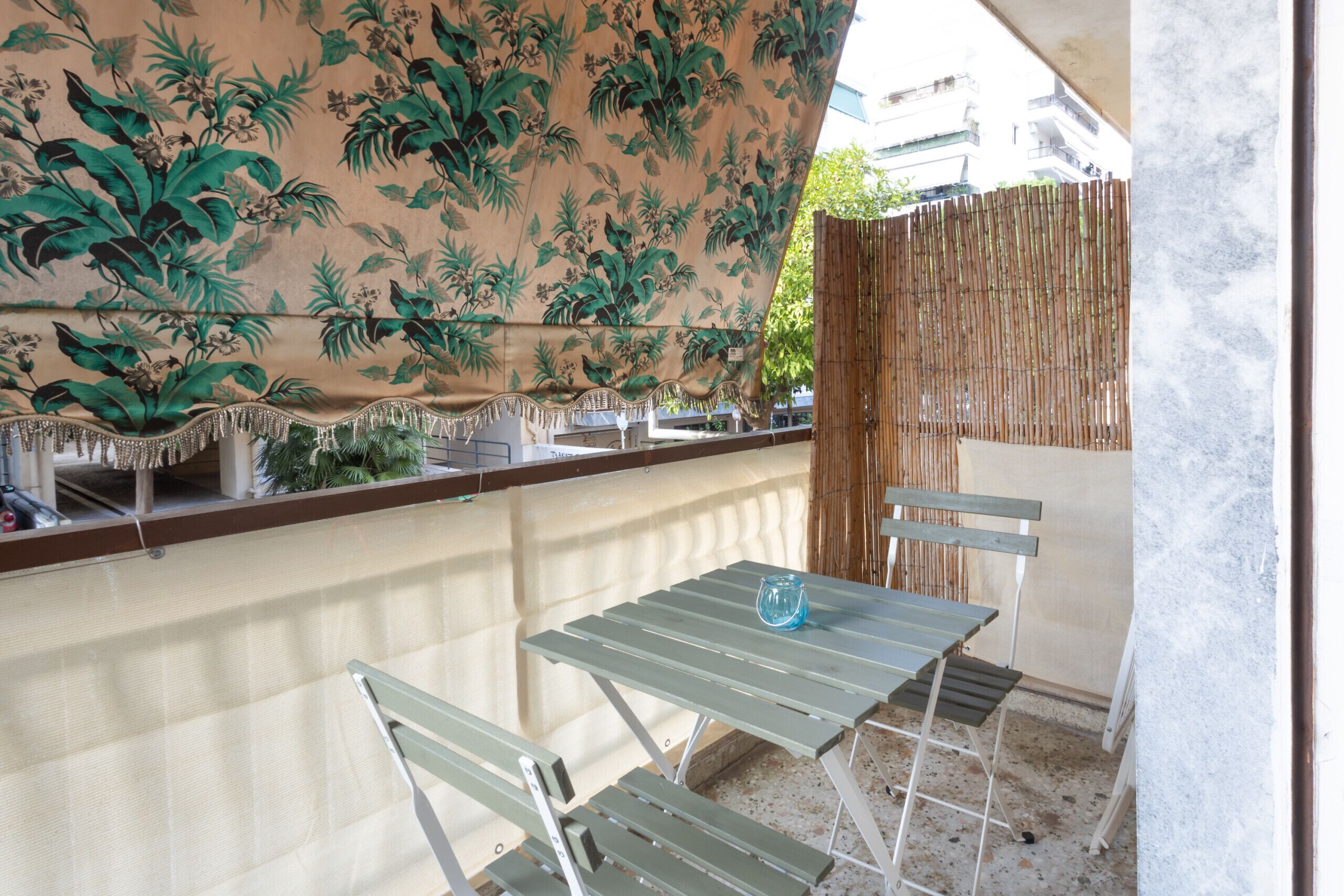 A balcony with a table and chairs, a decorative wall with a floral pattern, and a bamboo fence.