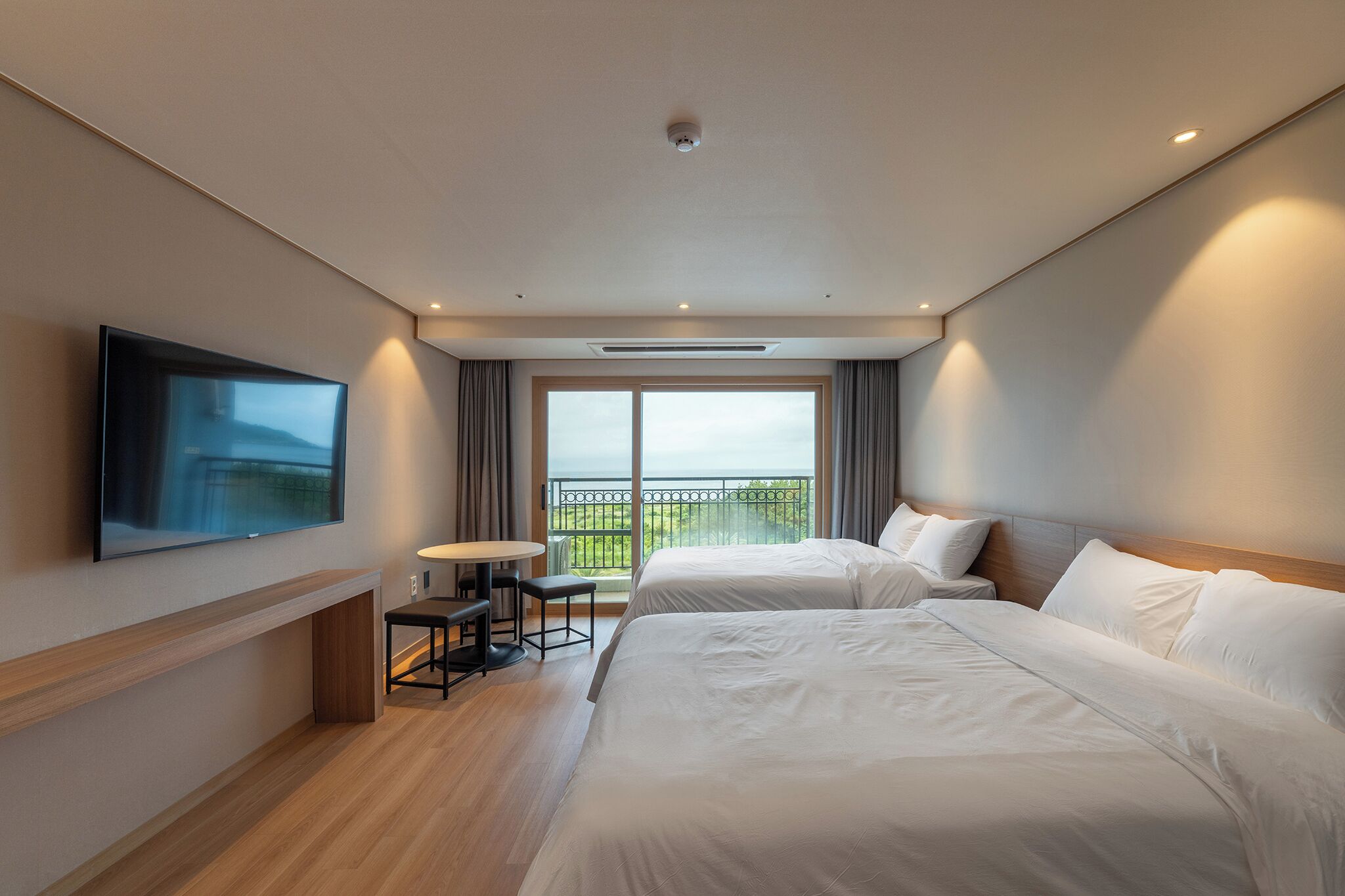 A hotel room with two beds, a TV, a small table, and a balcony with a view.