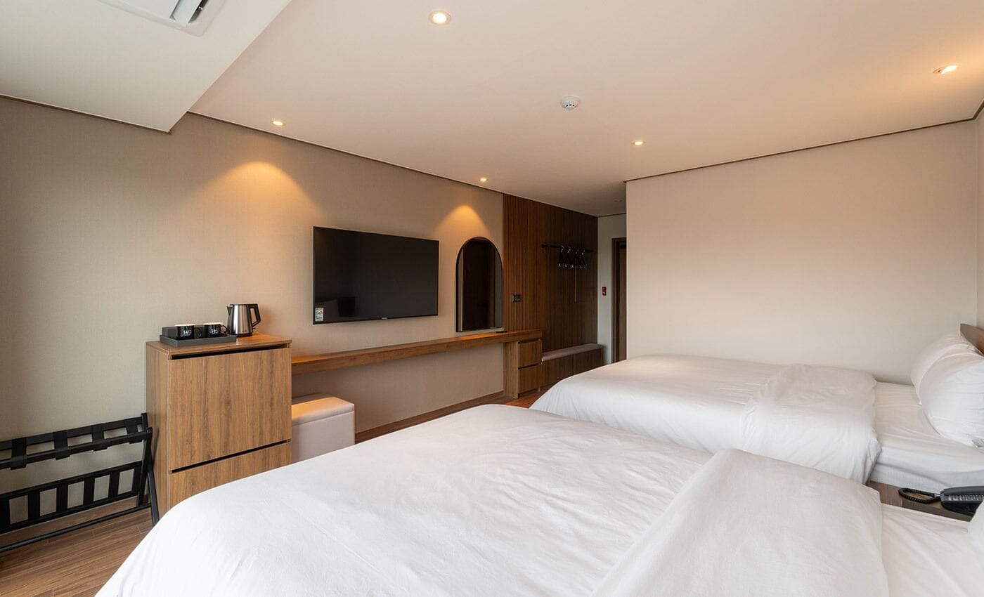 Een hotelkamer met twee bedden, een televisie, een houten kast en een douchegedeelte.