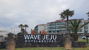 The Wave Jeju Hotel & Resort sign with a stone wall and palm trees.
