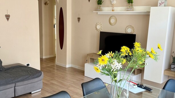 A modern living room with a glass dining table, grey sofa, and a fireplace with decorative items. - Modern and Cozy Oasis in the Heart of the City (Civitavecchia)