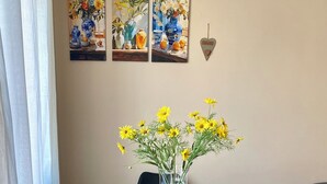 A dining area with a glass table, black chairs, and a vase of yellow flowers. There are three paintings on the wall above the table. - Modern and Cozy Oasis in the Heart of the City (Civitavecchia)