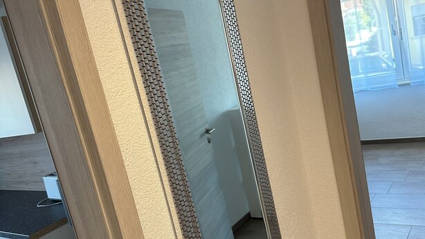 A room with a large mirror, a wooden cabinet, a trash bin, and a door leading to another room. - Fantastic vacation apartment (Altendorf)