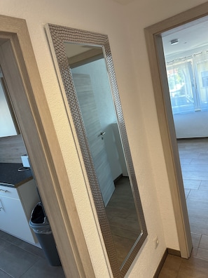 A room with a large mirror, a wooden cabinet, a trash bin, and a door leading to another room. - Fantastic vacation apartment (Altendorf)