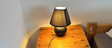 A wooden bedside table with a lamp, a drawer, and a power outlet.