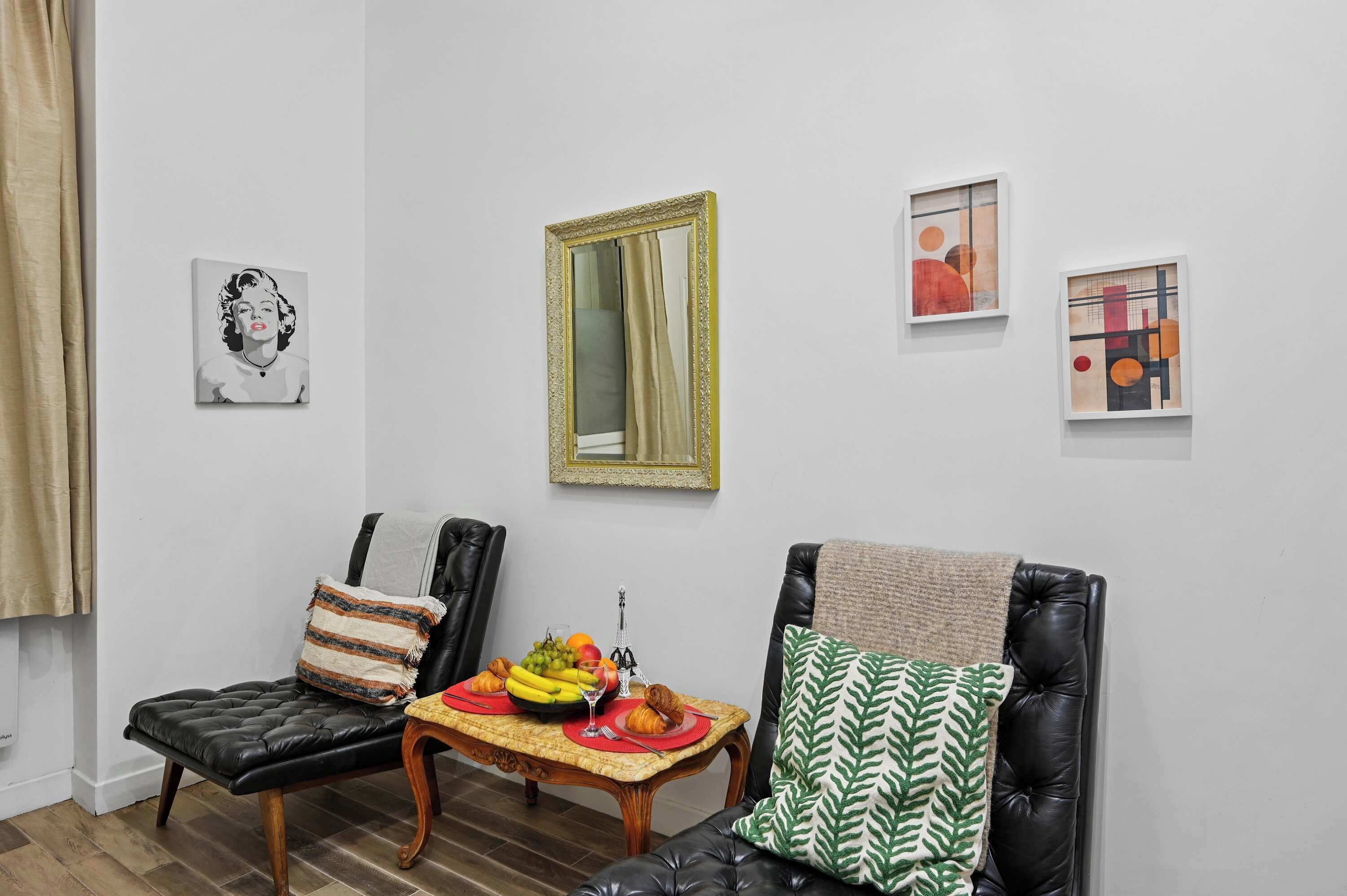 Una habitación con una mesa de comedor dispuesta con frutas y pasteles, dos sillas y un sofá con cojines estampados.