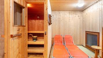 Un sauna avec des murs en bois, un banc, une étagère avec un seau et une petite table.