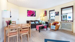 Un salon comprenant une table à manger en bois, des chaises, un canapé, une table basse et une fenêtre avec des stores.