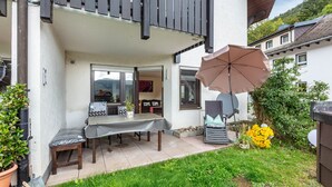 Une terrasse extérieure avec une table et des chaises, un banc en bois, une plante en pot et un arrangement floral jaune.