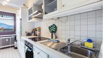 Een keuken met een roestvrijstalen spoelbak, witte kastjes, een raam met uitzicht en een radiator.