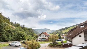 Un quartier résidentiel avec des maisons, des voitures garées et un paysage vallonné en arrière-plan.
