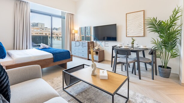 A modern hotel room with a bed, a sofa, a dining area, and a large window offering a city view. - Cozy Studio with Peaceful Community Views, Just Steps from Parks & Circle Mall (Dubai)