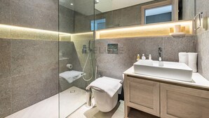 A modern bathroom with a glass-enclosed shower, a white sink, and wooden cabinets. - Cozy Studio with Peaceful Community Views, Just Steps from Parks & Circle Mall (Dubai)