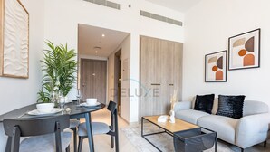 A modern living room with a dining area, a sofa, a coffee table, and a plant. - Cozy Studio with Peaceful Community Views, Just Steps from Parks & Circle Mall (Dubai)