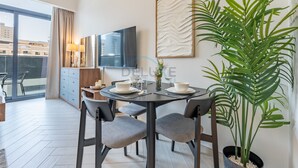 A modern dining area with a round table, grey upholstered chairs, and a large potted plant. - Cozy Studio with Peaceful Community Views, Just Steps from Parks & Circle Mall (Dubai)