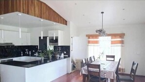 A modern kitchen with white cabinetry, a black countertop, and a dining area with a table and chairs. - Bulla Villas & Suites (Nadi)