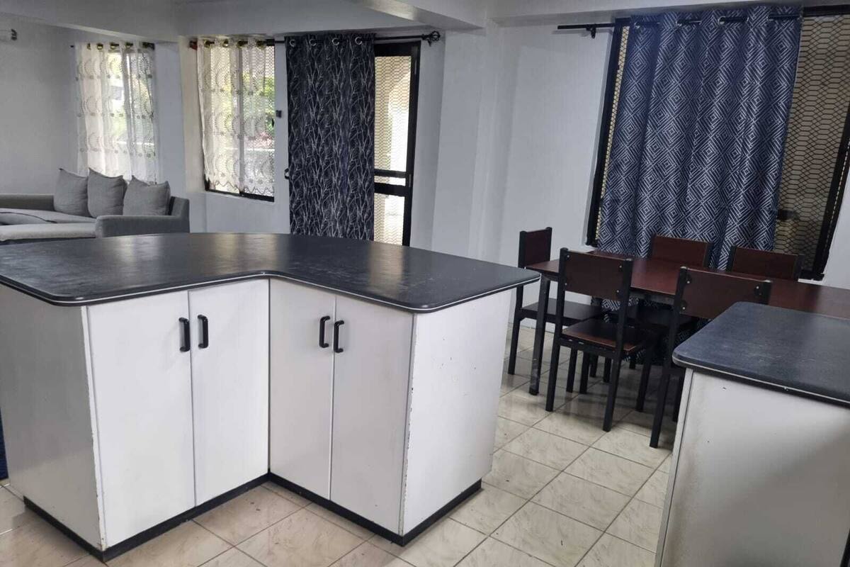 A kitchen with white cabinets, a black countertop, and a dining area with wooden chairs and a table.