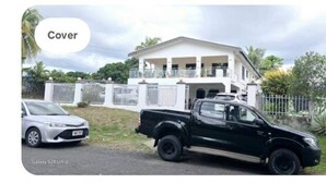 A black pickup truck parked in front of a large white house with a balcony. - Bulla Villas & Suites (Nadi)