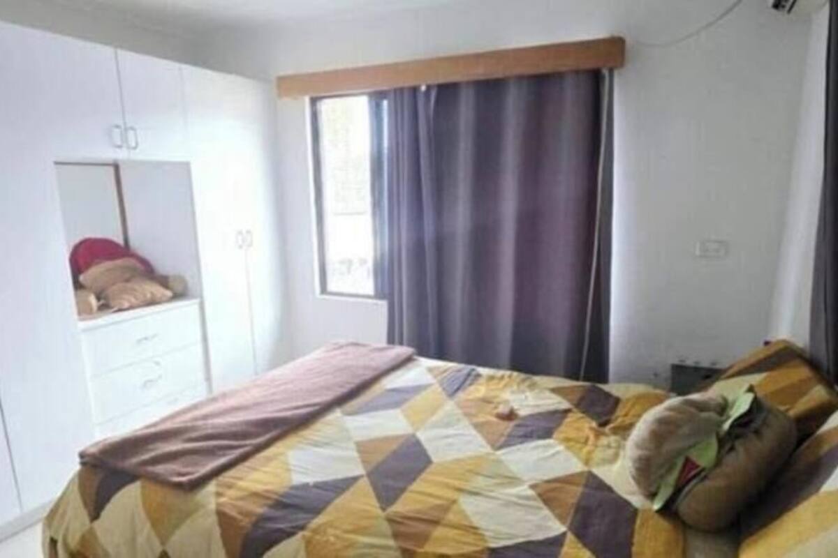 A bedroom with a bed, a wardrobe, a mirror, and a window with curtains.