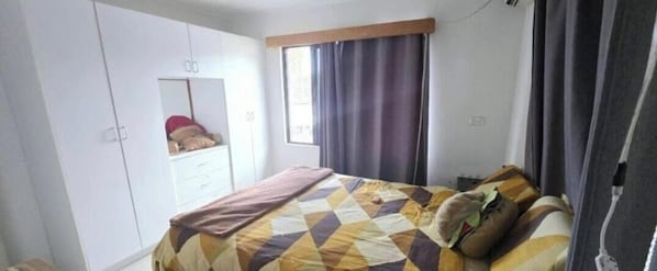 Un dormitorio con cama, armario, espejo y ventana con cortinas.