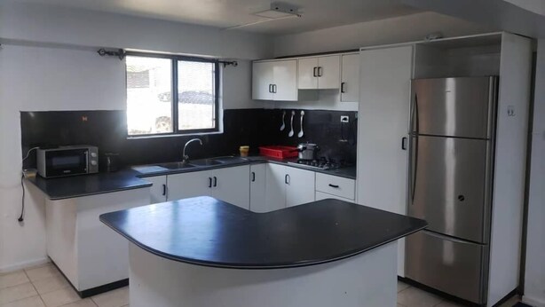 A modern kitchen with white cabinets, a black countertop, a stainless steel refrigerator, and a microwave. - Bulla Villas & Suites (Nadi)