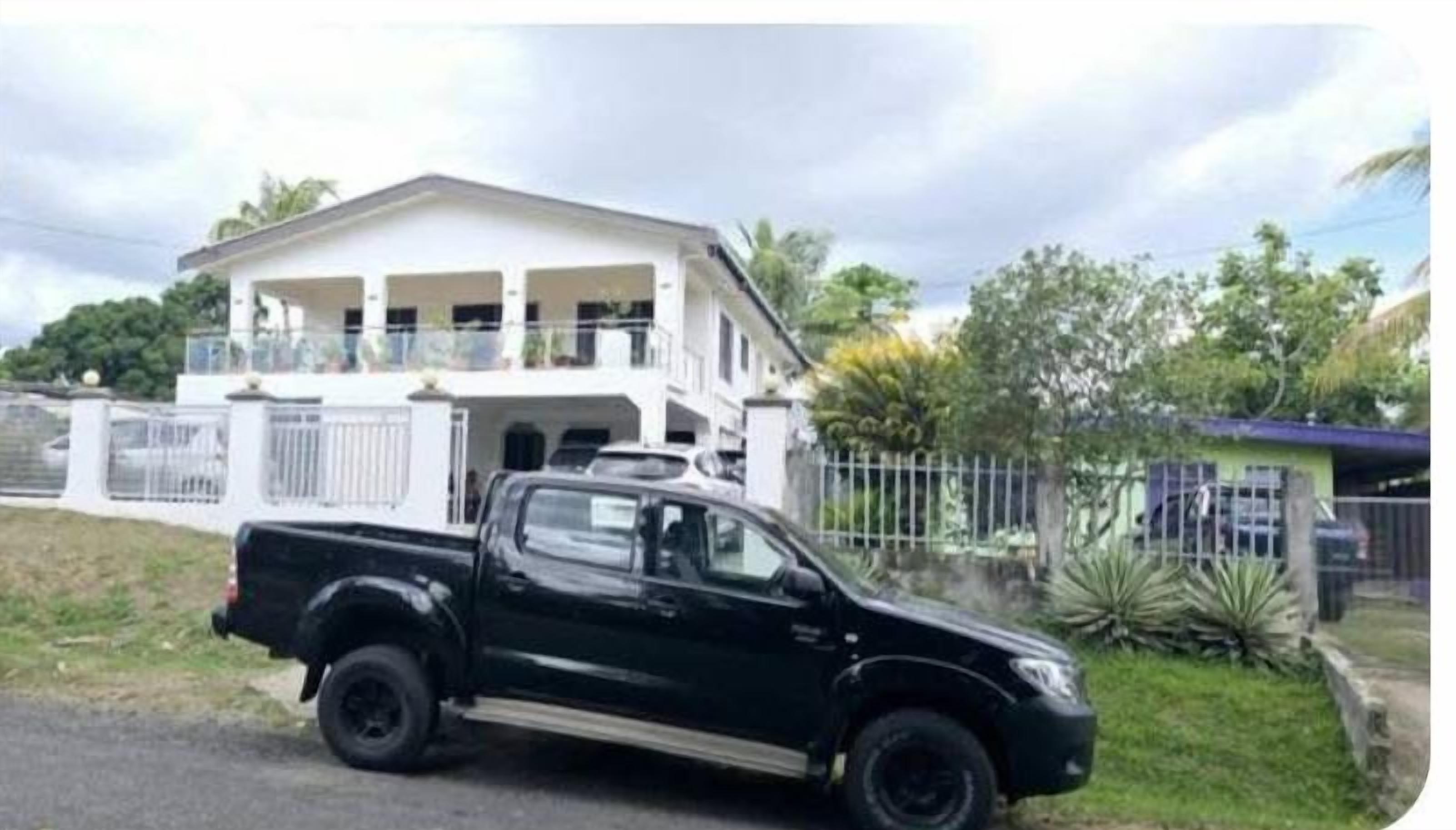 Een zwarte pick-up truck geparkeerd voor een groot wit huis met een balkon.