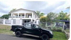 Una camioneta negra estacionada frente a una amplia casa blanca con balcón.