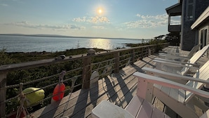 A wooden deck with lounge chairs overlooking a body of water, a stone building, and a clear sky.
