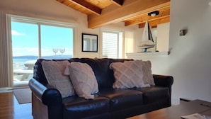 A living room with a dark leather sofa, two decorative pillows, a wooden coffee table, and a sailboat model on the wall.