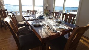 A dining table set for six with a view of the sea through large windows.