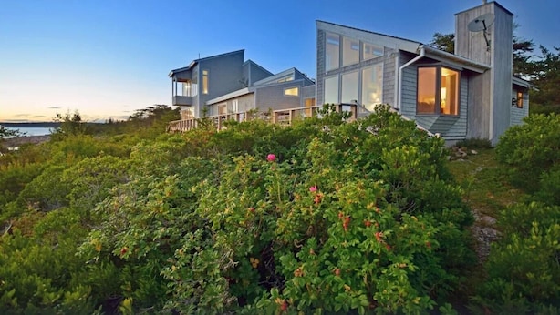 A modern coastal house with multiple rooms, a large deck, and a satellite dish.