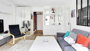 A modern living room with a grey sofa, a black chair, a white coffee table, and a white cabinet with glass doors. - Cosy Studio - 2P - Trocadero (Paris)