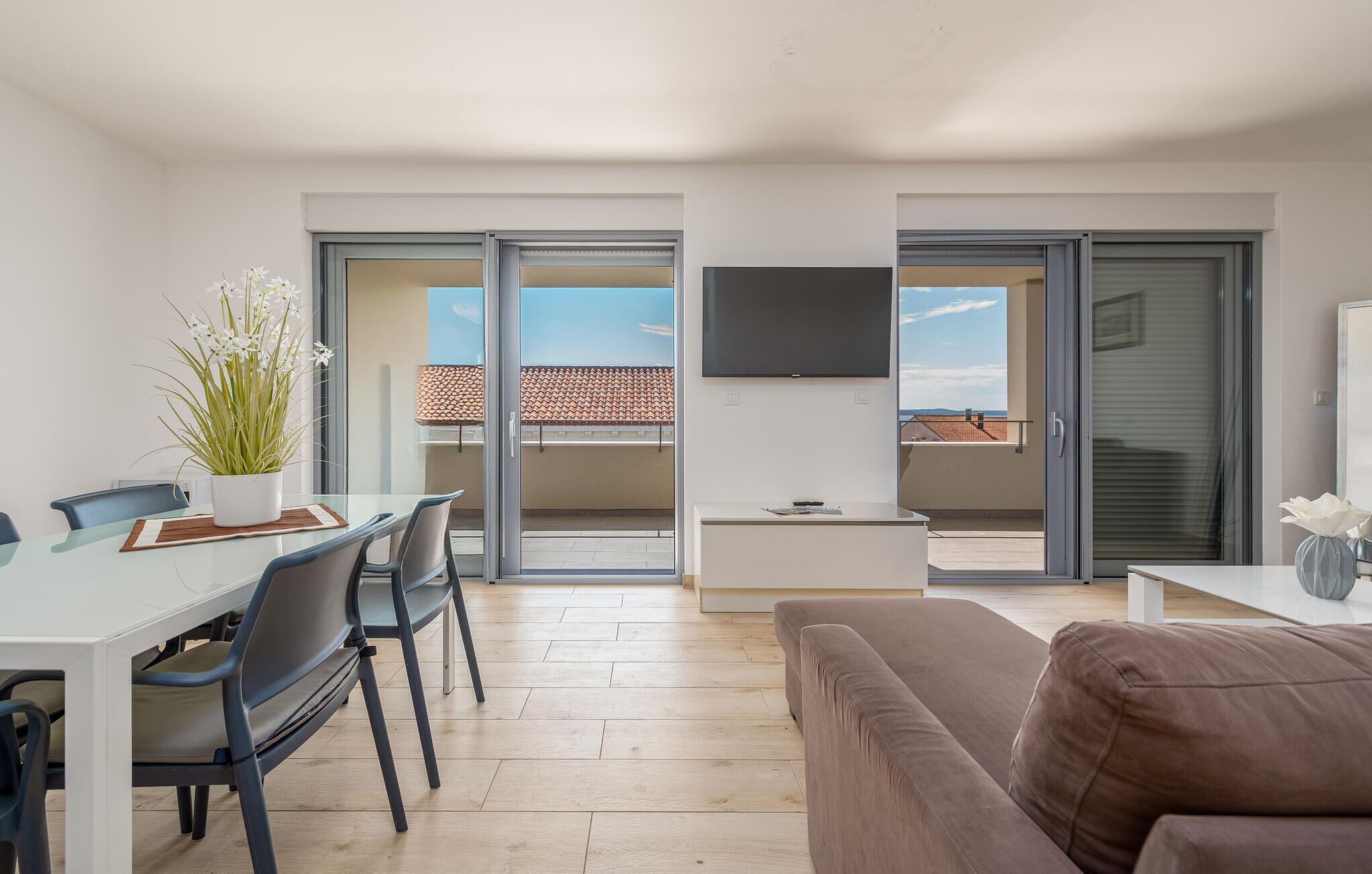 A modern apartment with a dining area, a sofa, a TV, and a balcony with a tiled roof.