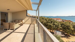 A balcony with wicker furniture, a view of the sea, and a white van parked nearby. - 2 bedroom lovely apartment in Kozino (Kozino)