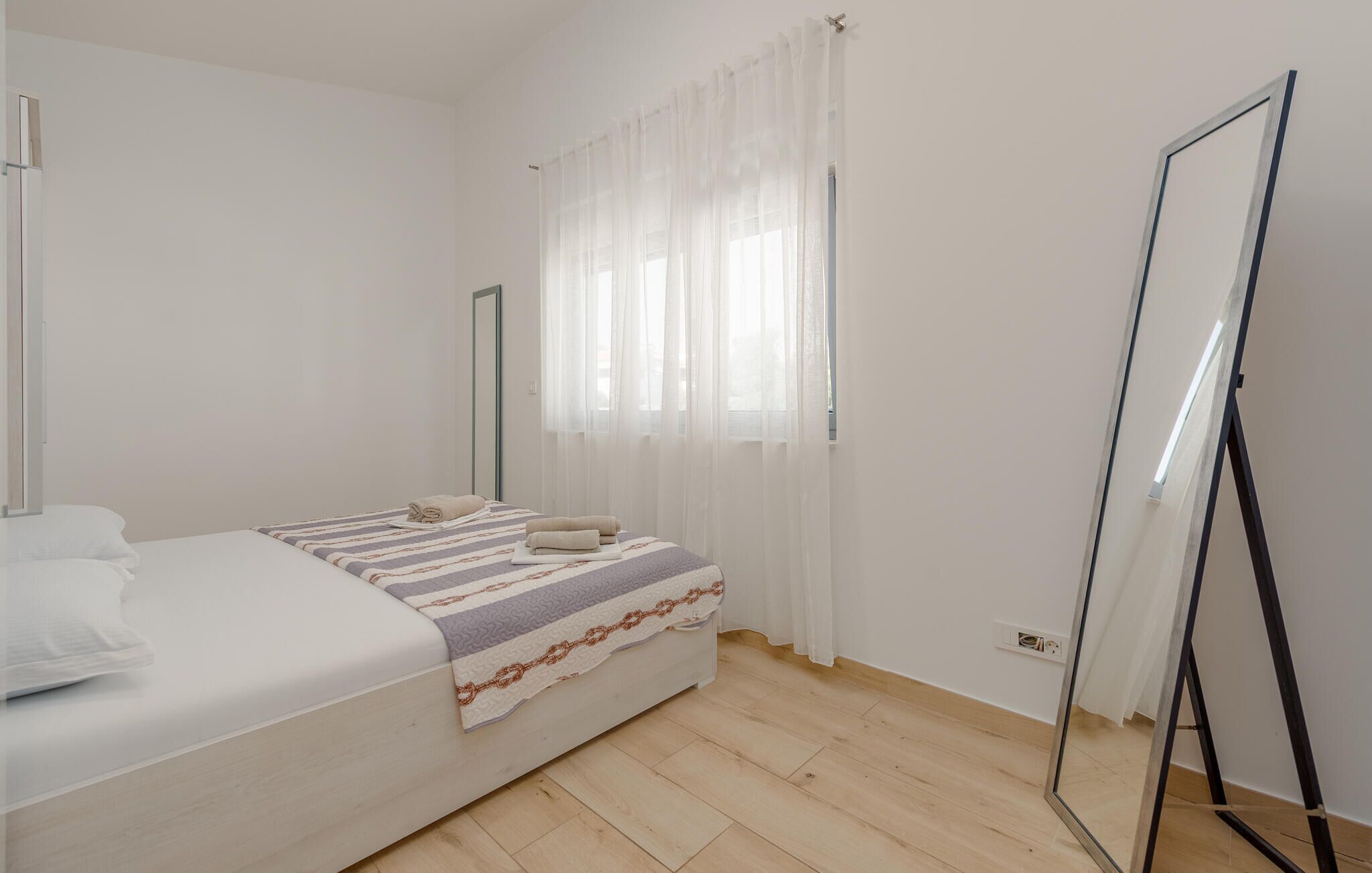 Ein Schlafzimmer mit einem Bett, einem Spiegel und einem Fenster mit durchsichtigen Vorhängen.