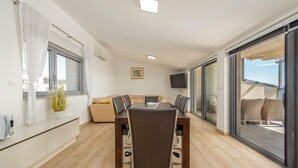 A modern living room with a dining table, sofa, and a large sliding glass door leading to a balcony. - 2 bedroom lovely apartment in Kozino (Kozino)